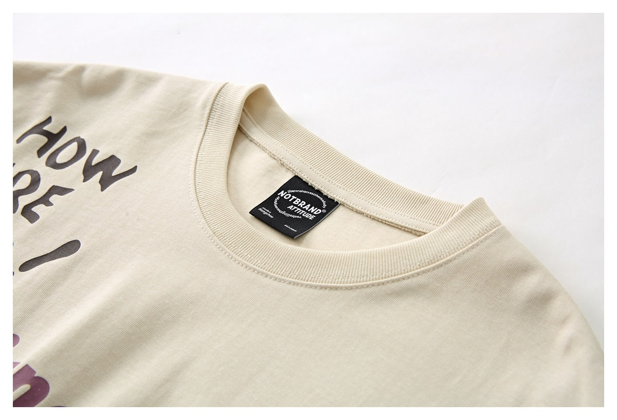 Close-up of a cream T-shirt's ribbed crew neck and black woven label, with part of the dark printed design visible.