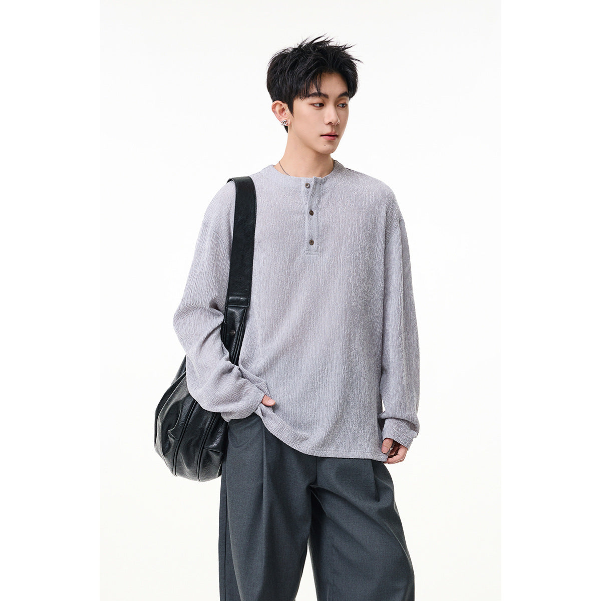 Model wearing a light gray textured long-sleeve henley with a short button placket and dark trousers, front view.