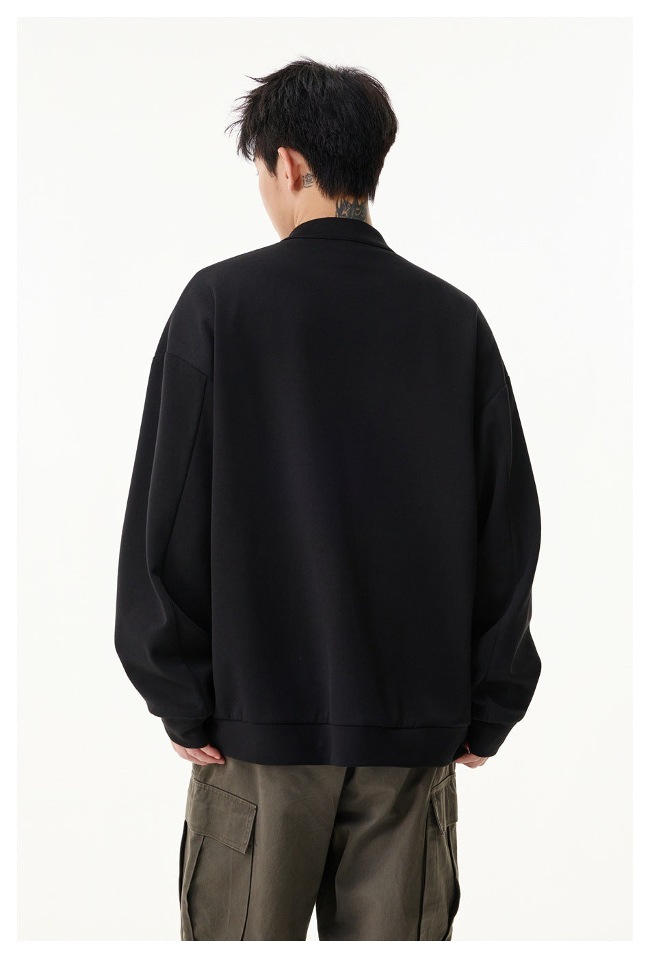 Rear view of a model wearing a plain black jacket with a ribbed hem and olive cargo trousers.