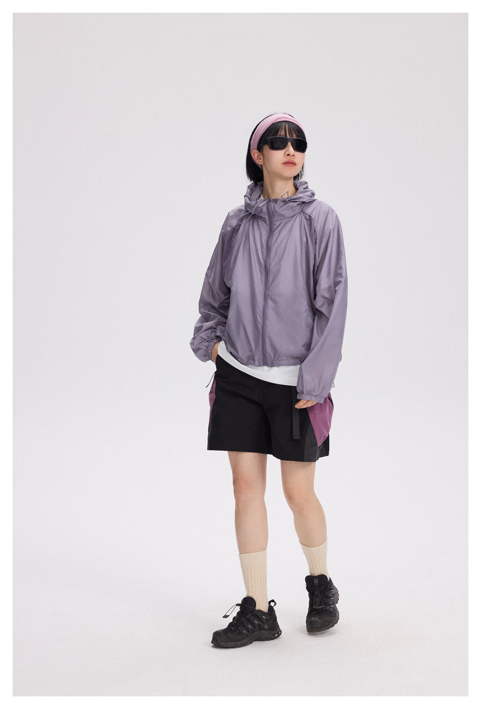 A model wears a lavender hooded jacket with black shorts and magenta side pockets.