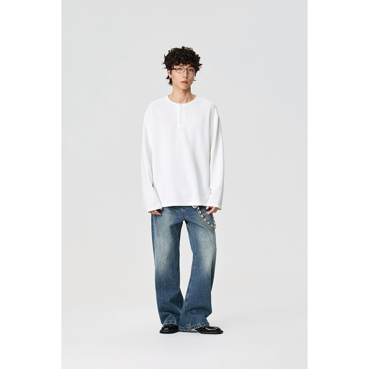 Full-length front view of a model wearing a white long-sleeve henley shirt and loose blue jeans.