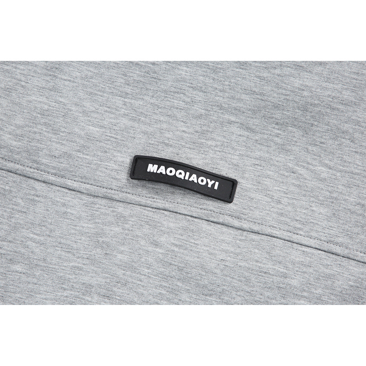 Close-up of a black rectangular MAOQIAoyi label on gray heathered jacket fabric.