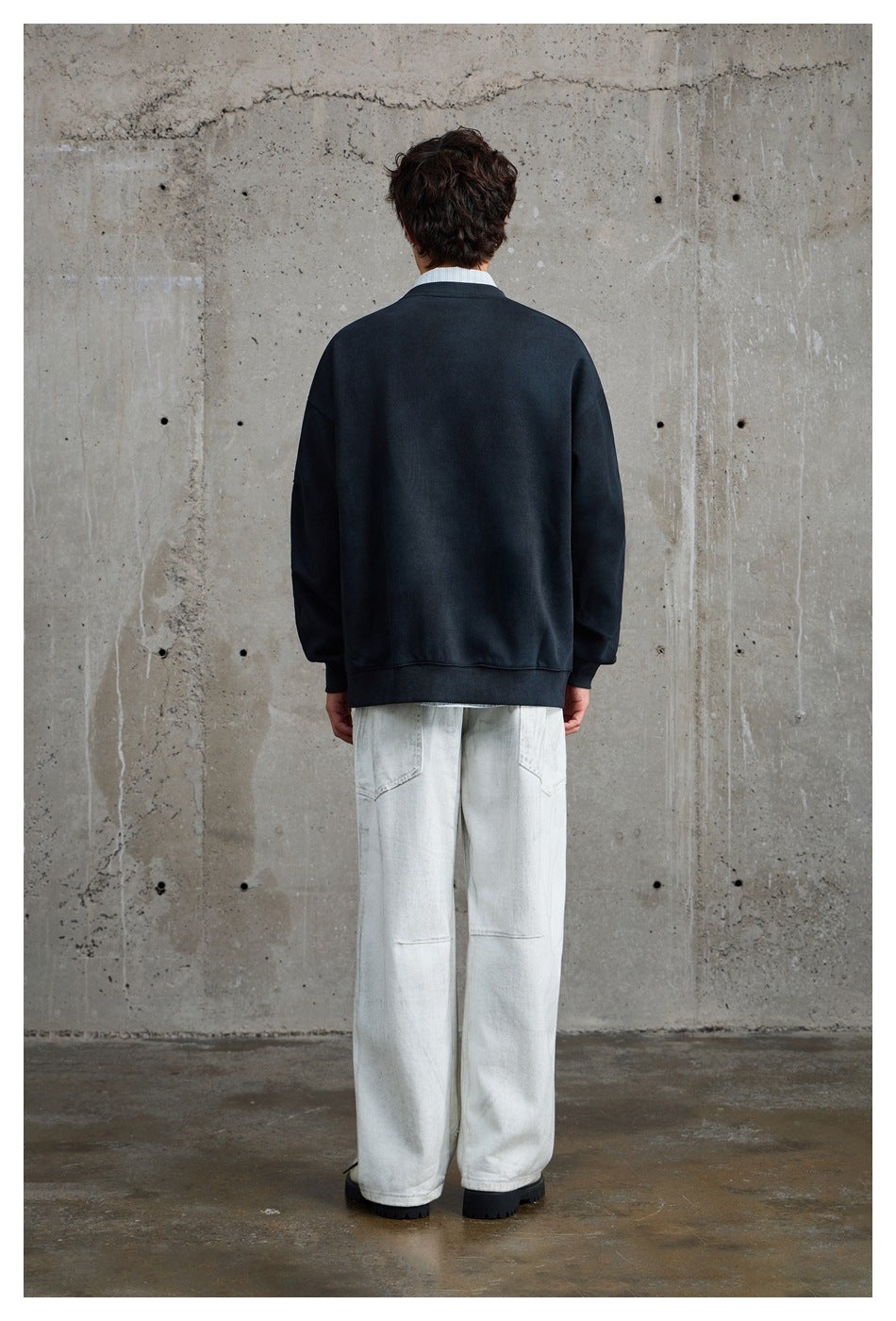 Back view of a model wearing a plain dark navy crewneck sweatshirt with loose white trousers.