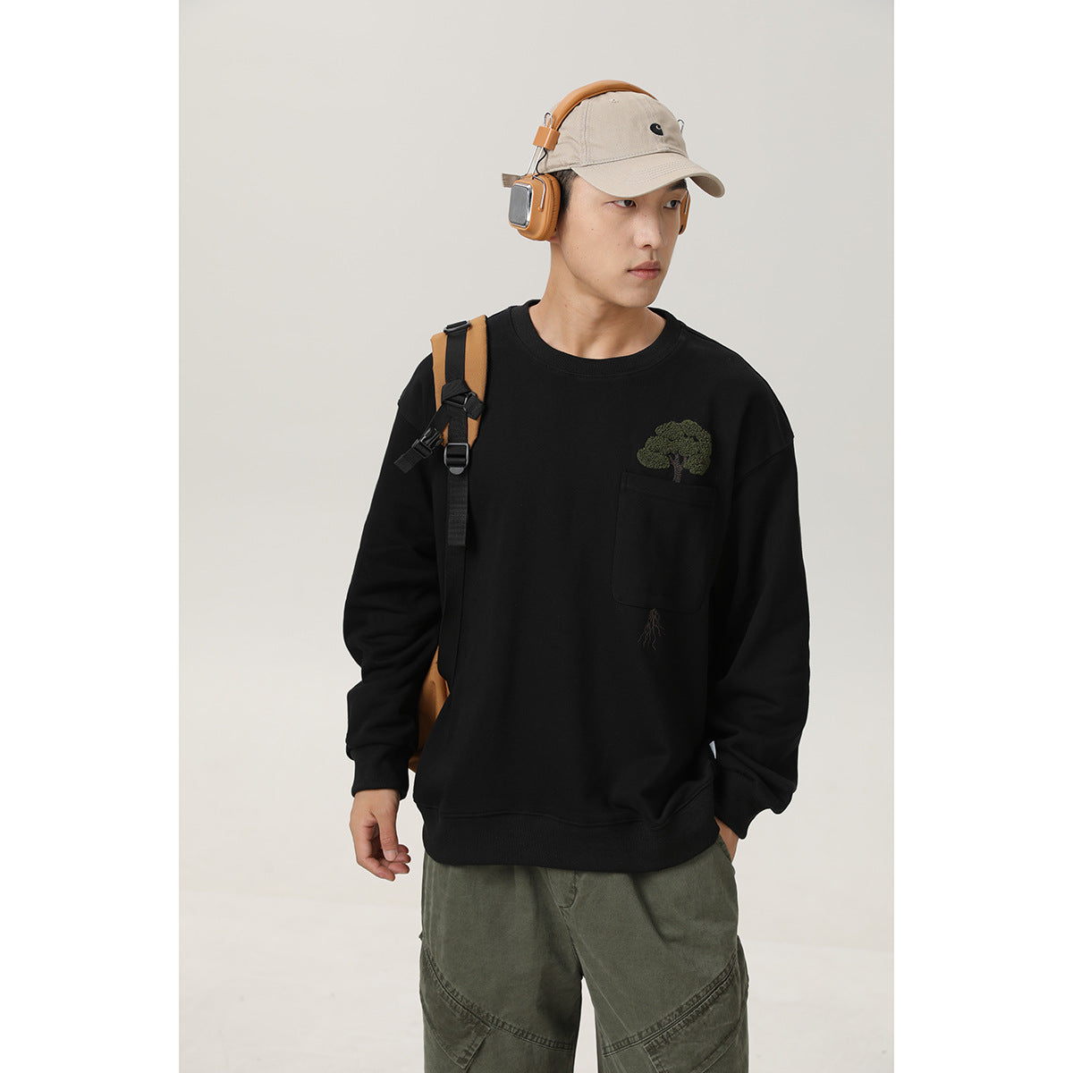 Model wearing a black crewneck sweatshirt with a chest pocket and embroidered tree design.
