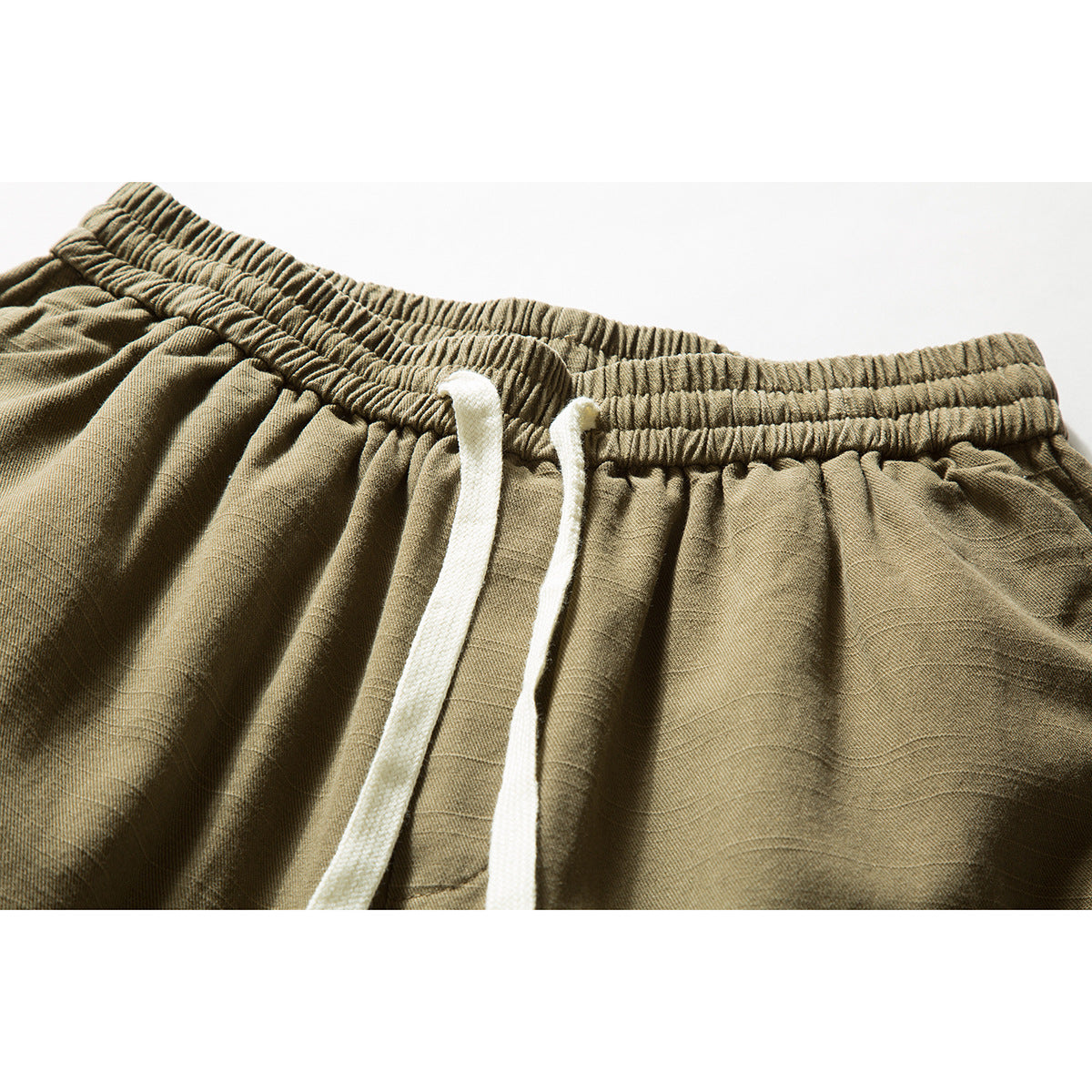 Close-up of olive-khaki trousers showing the gathered elastic waistband and two white drawstrings.