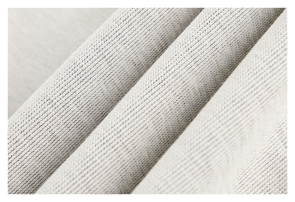 Close-up of pale ivory knit fabric arranged in diagonal folds, highlighting its textured stitch pattern.