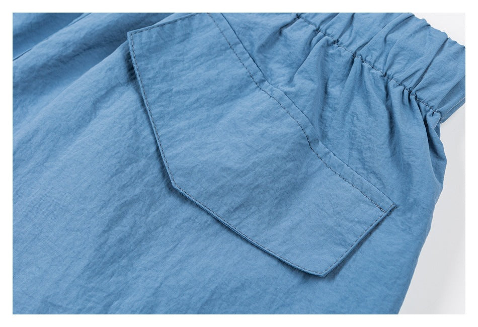 Close-up of blue shorts showing a large stitched back pocket beside the elastic waistband.