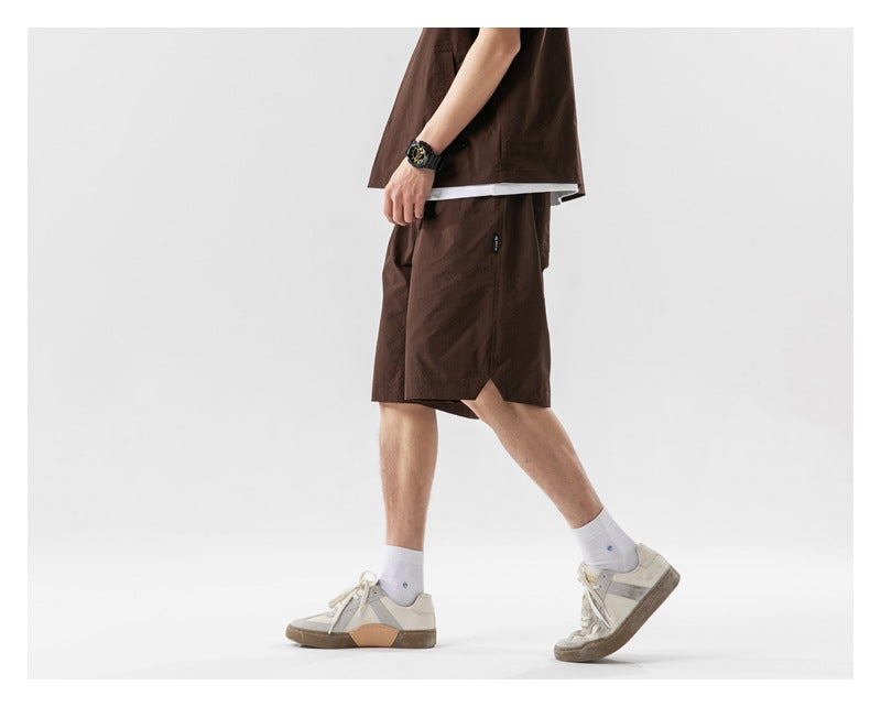 Cropped side view of a model wearing dark brown knee-length shorts with a matching top and white sneakers.