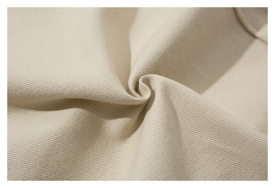Close-up of cream-colored fabric gathered into folds, showing a fine diagonal ribbed texture.