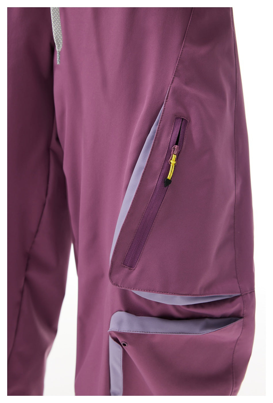 Close-up of mauve cargo pants showing a zippered thigh pocket with a yellow pull and pale contrast trim.