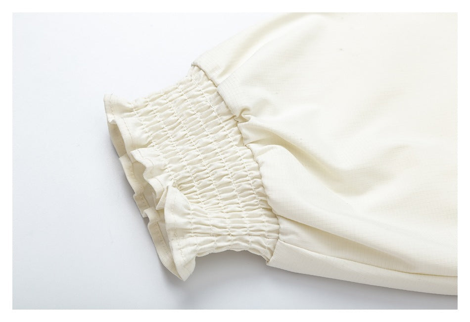 Close-up of an ivory garment sleeve with a wide elastic-shirred ruffle cuff.