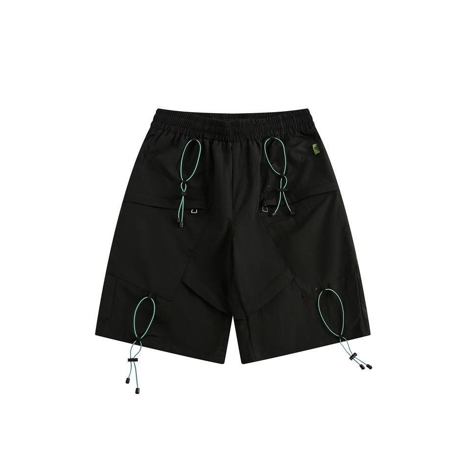 Black knee-length shorts, front view, with teal toggle cords, angled flap panels and an elastic waistband