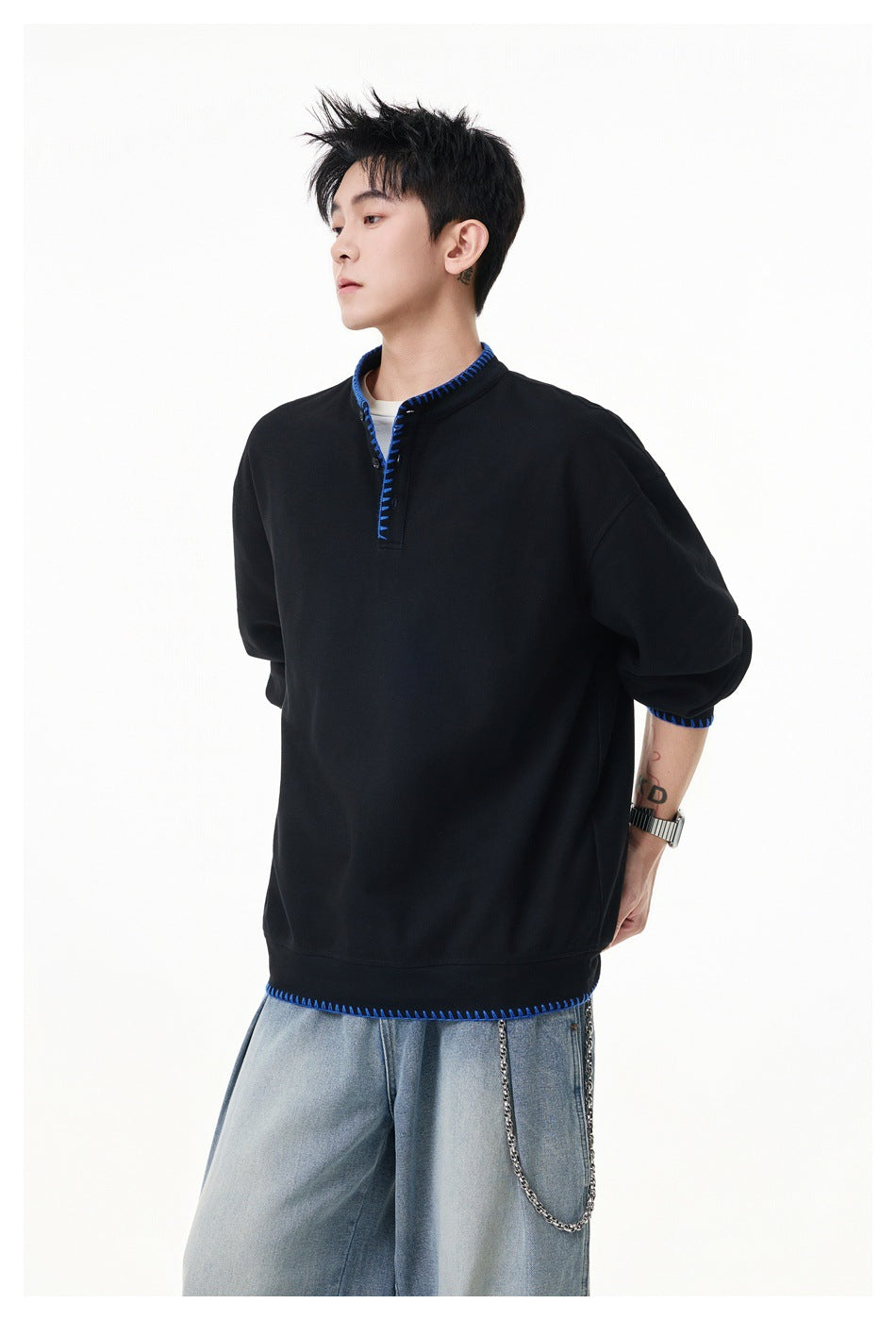 Model wearing a black oversized pullover with bright blue contrast stitching at the collar, placket, cuffs and hem.