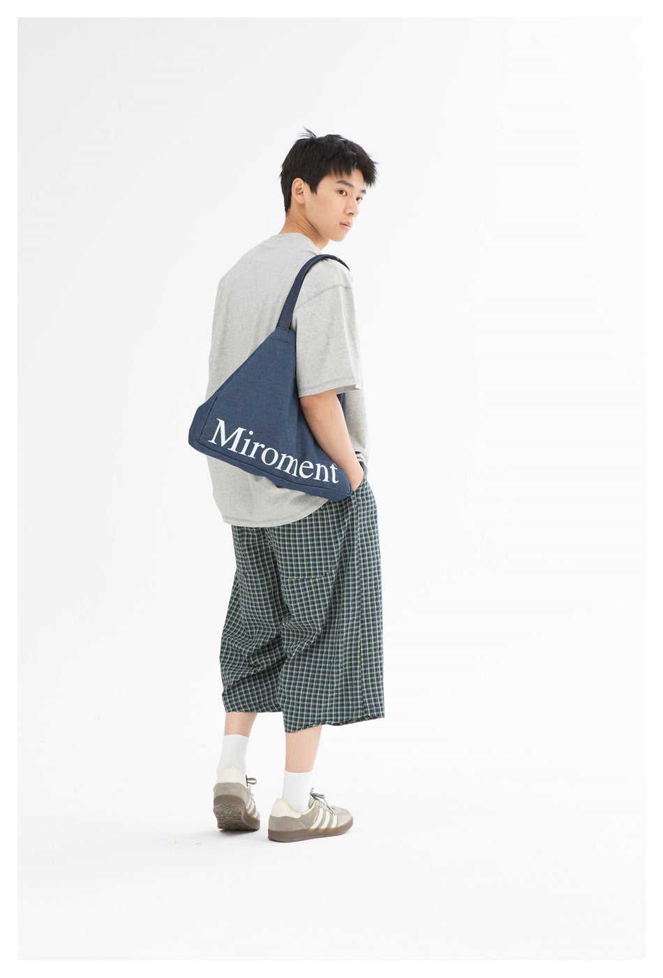 Model shown from behind in a gray T-shirt and plaid shorts, carrying a blue shoulder bag.
