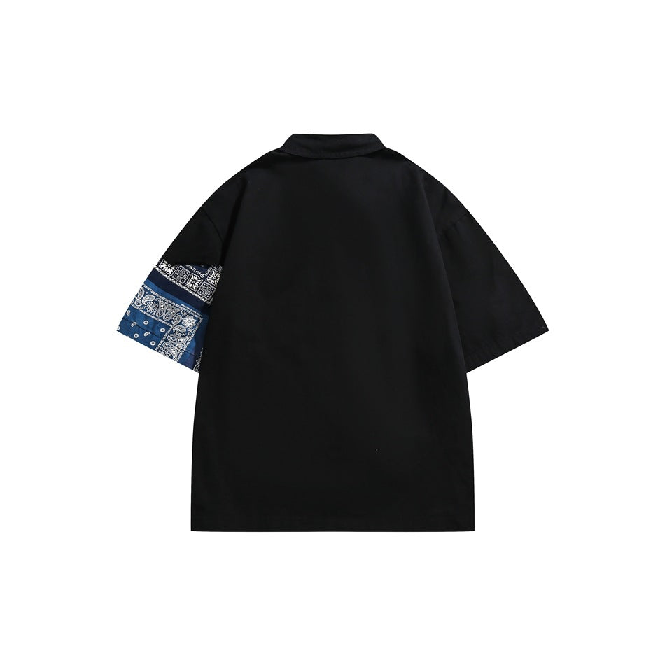 Back view of a black short-sleeve collared shirt with a blue bandana-print panel on one sleeve.