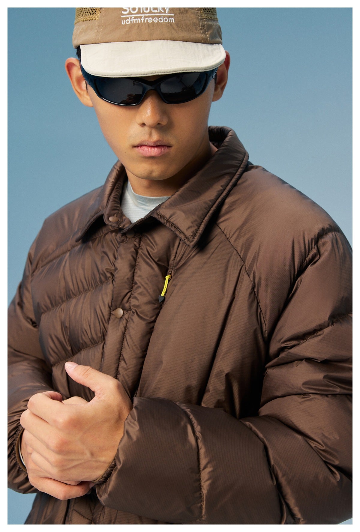 Close view of a model wearing a dark brown quilted jacket with a collar, snap closure, and yellow zipper pull.