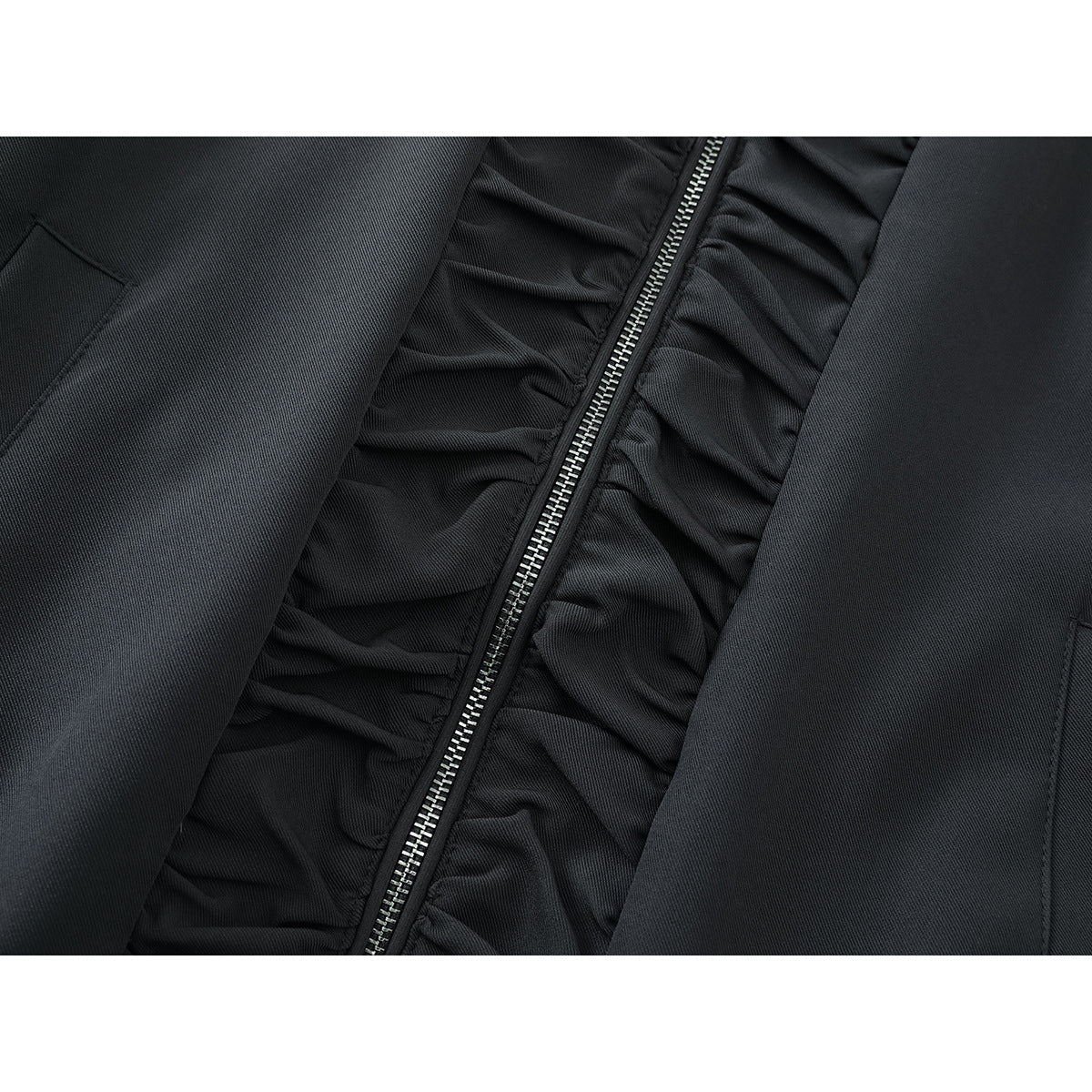 Close-up of a charcoal jacket’s silver zipper, gathered front trim, and welt pocket.
