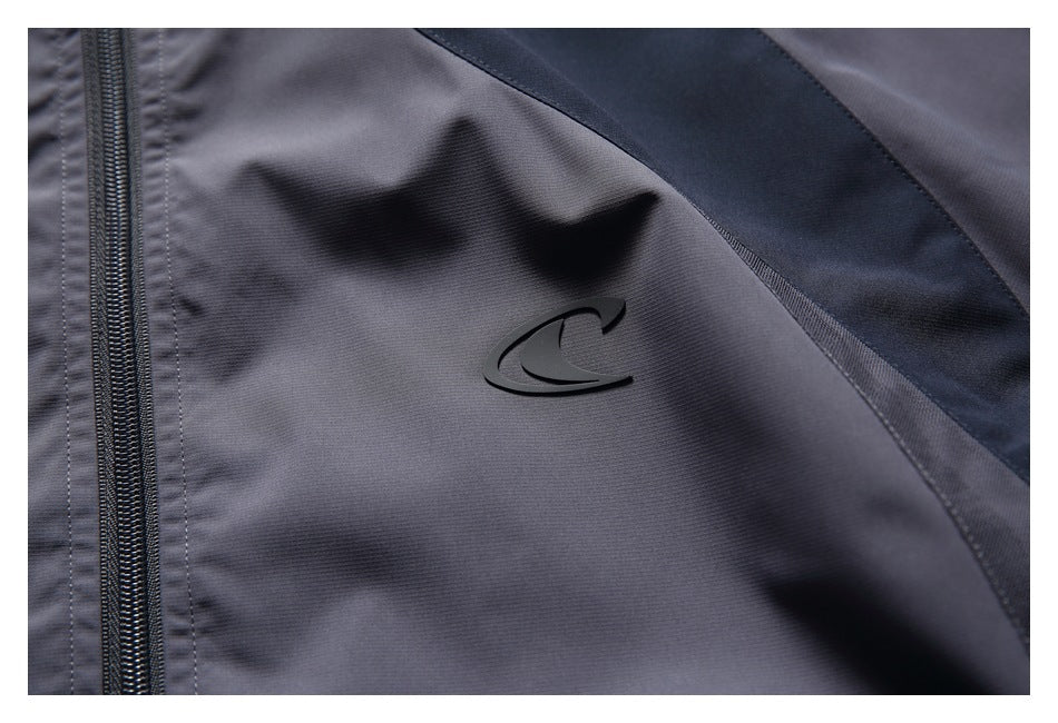 Close-up of a small black emblem on the charcoal-gray jacket beside the zipper and a dark contrast panel.