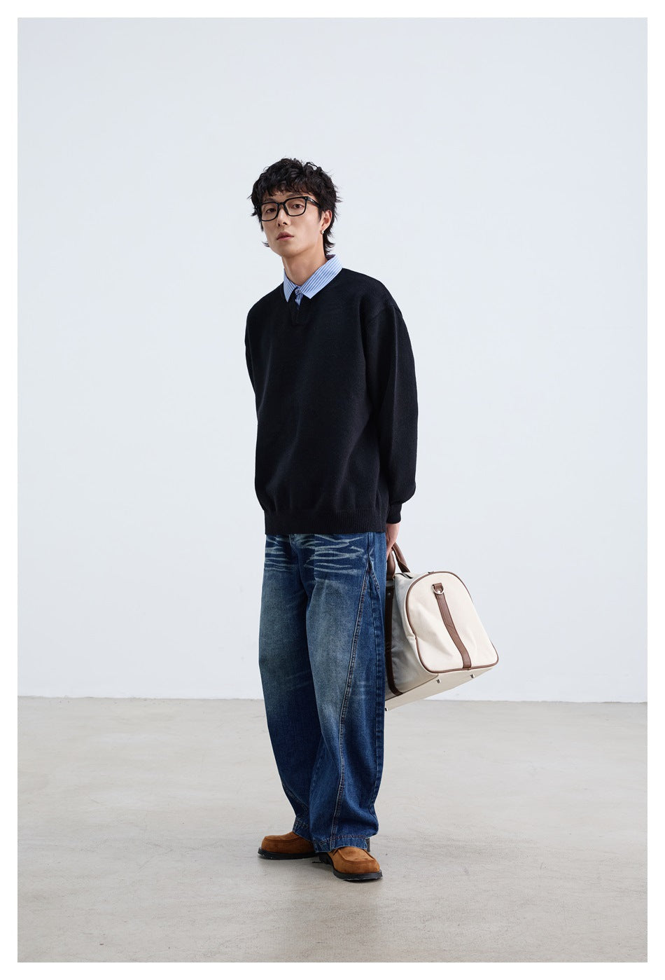 Model in a black sweater with striped collar, wide-leg jeans and a canvas duffel bag, angled view