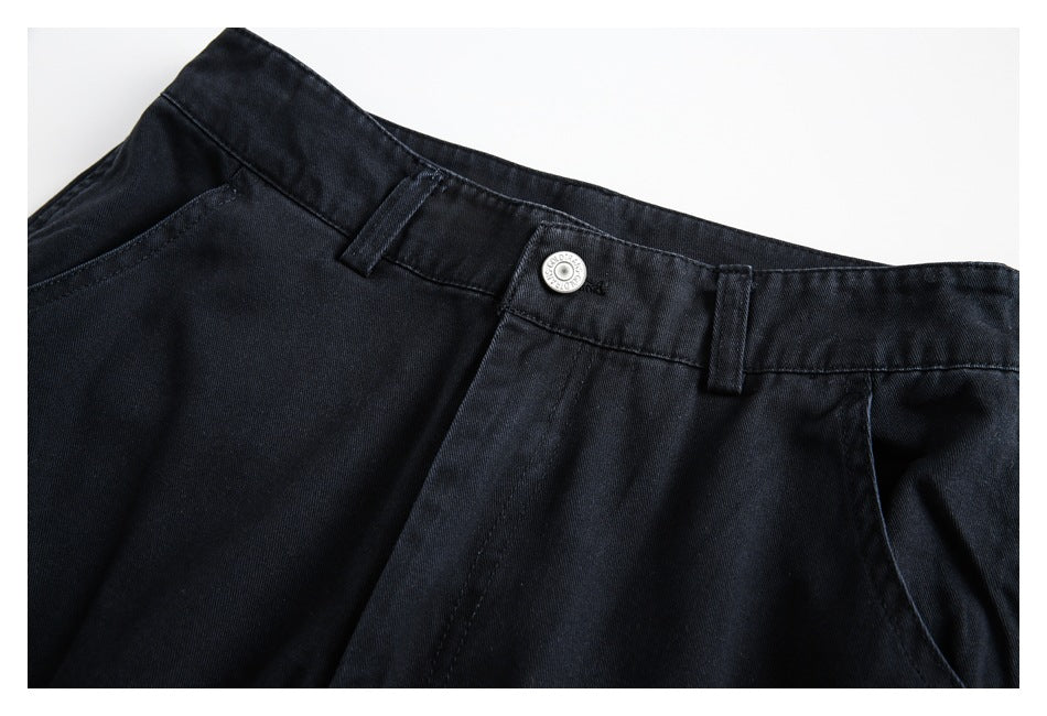 Close-up of black pants showing the waistband, button, belt loops, fly seam, and curved front pocket.