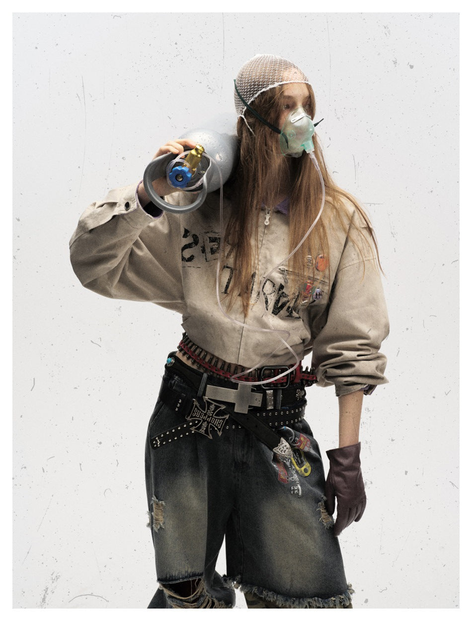 Model wearing a beige graphic jacket with purple collar, dark distressed denim shorts, gloves and layered belts.