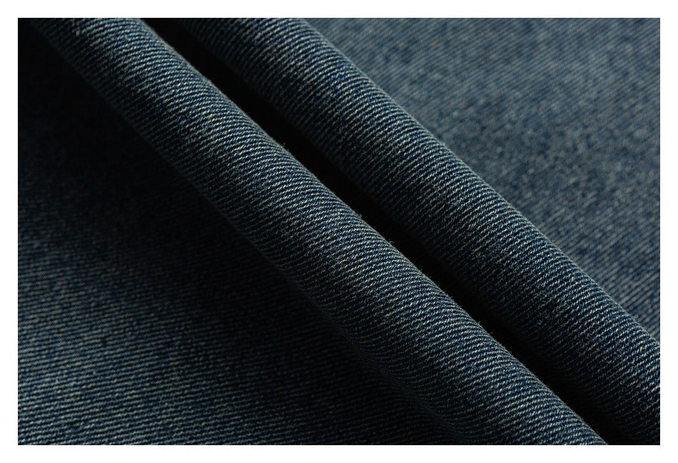 Close-up of dark blue denim fabric draped in folds, showing its diagonal weave.