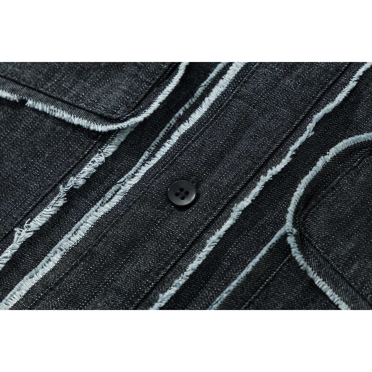Macro view of dark denim shirt panels with pale frayed stitching and a black button.