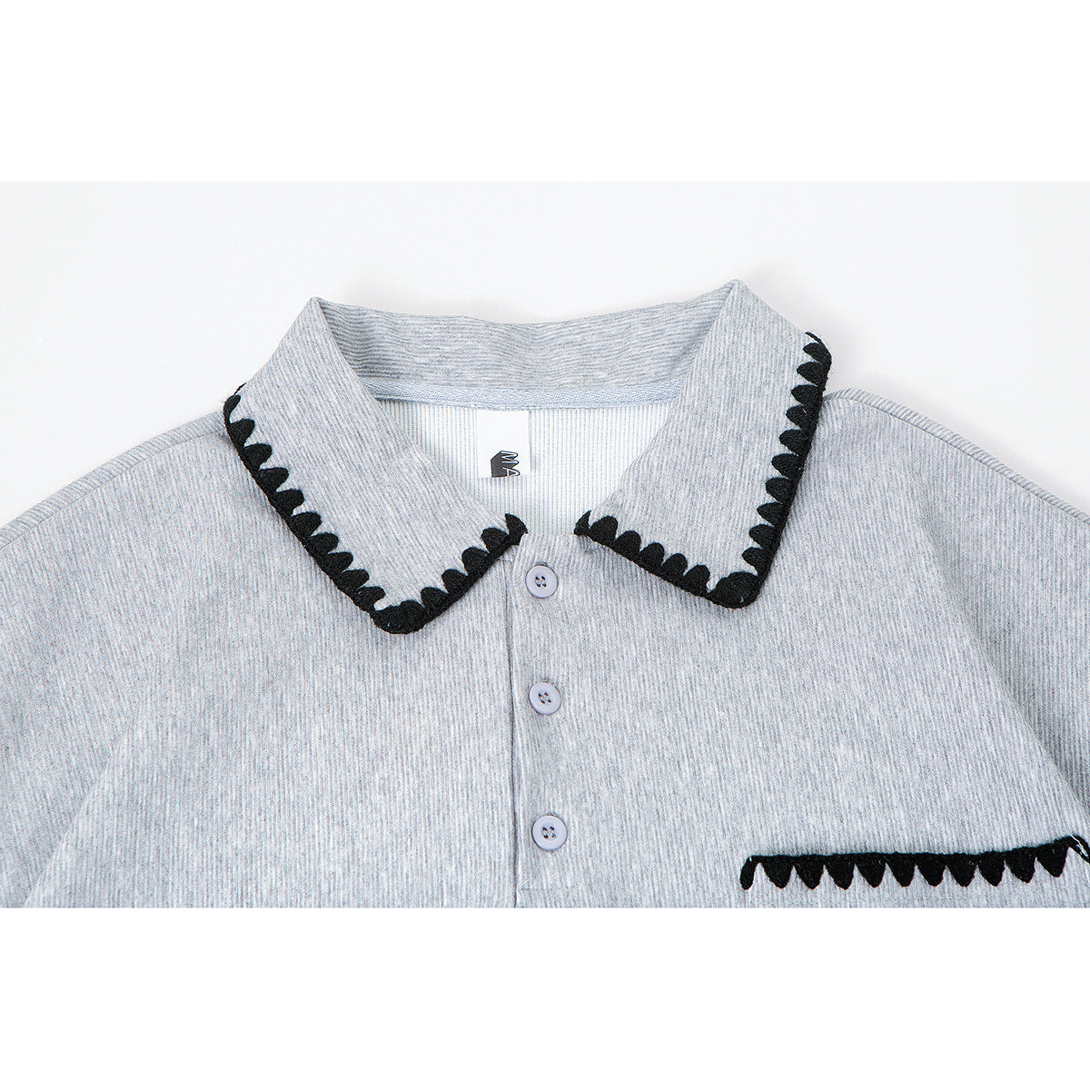 Close-up of a light gray short-sleeve polo shirt with black scalloped trim on the collar and chest pocket.