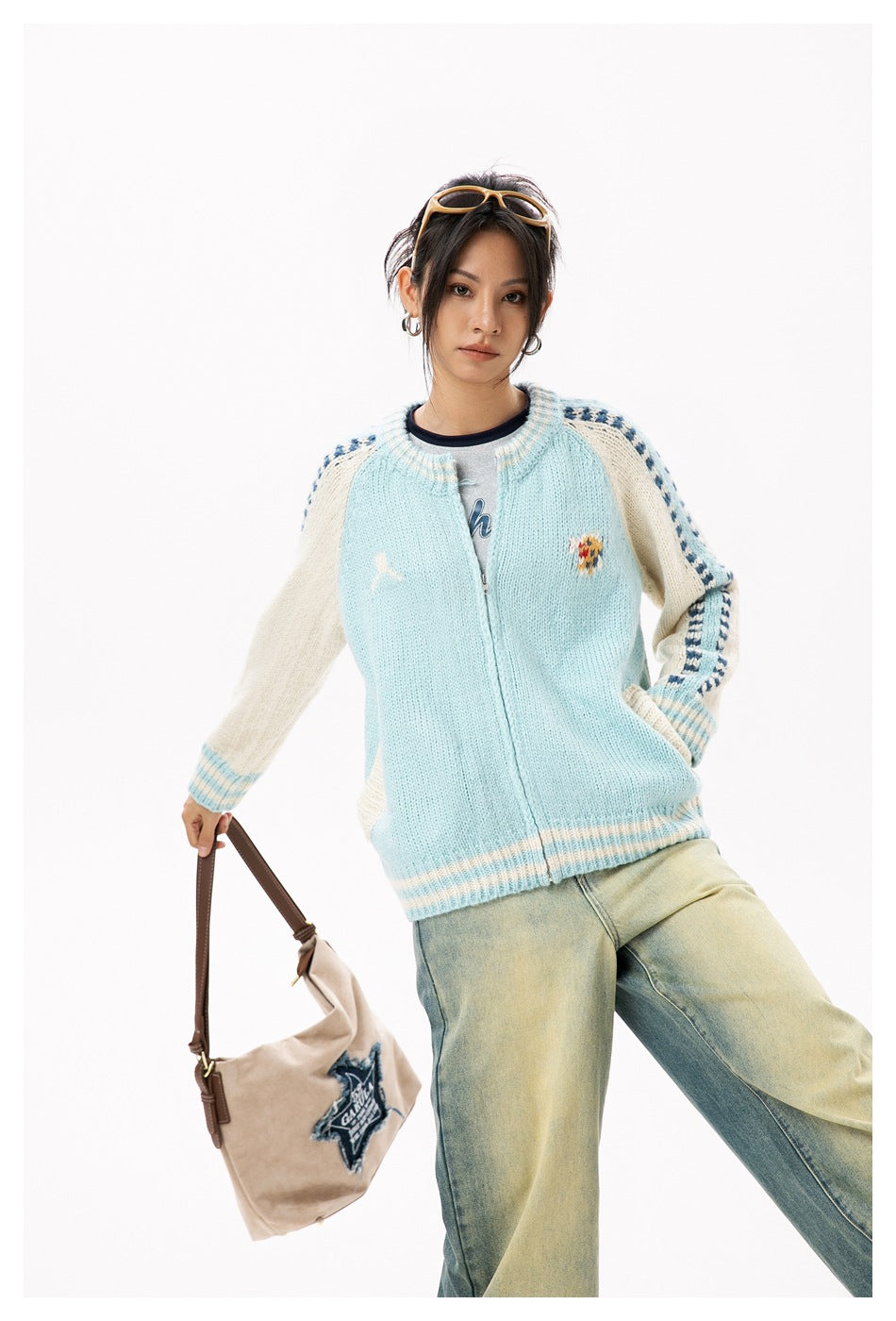 Model wearing a pale blue zip-front knit cardigan with cream raglan sleeves, navy trim, and small chest motifs.