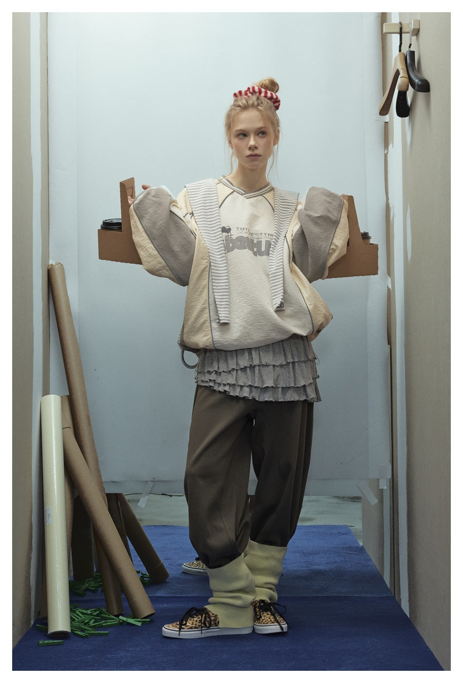 Model wearing a cream graphic sweatshirt with contrast piping and a gray striped garment draped over her shoulders.