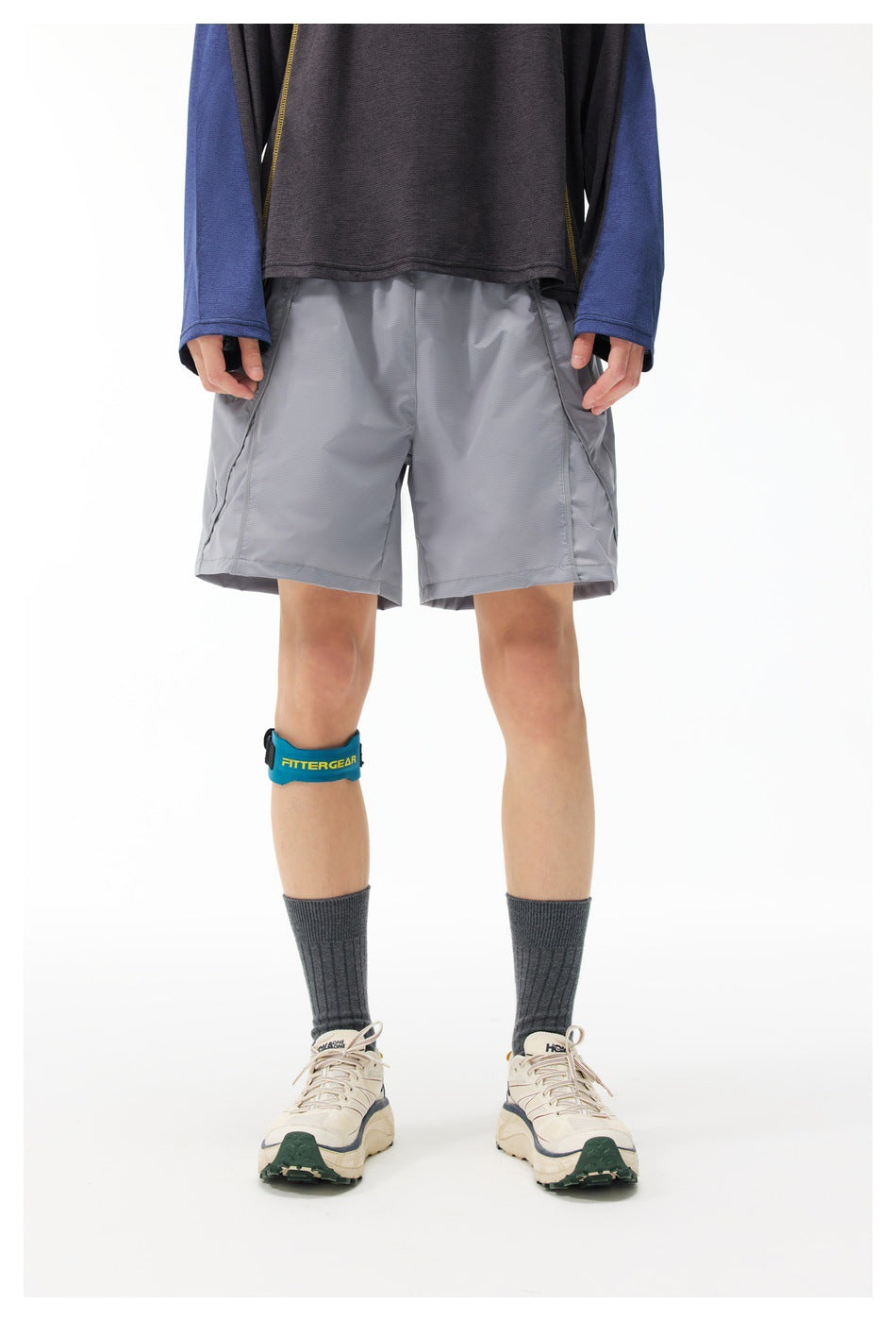 Front view of a model wearing gray athletic shorts with side pockets, a dark top, and a blue branded knee strap.