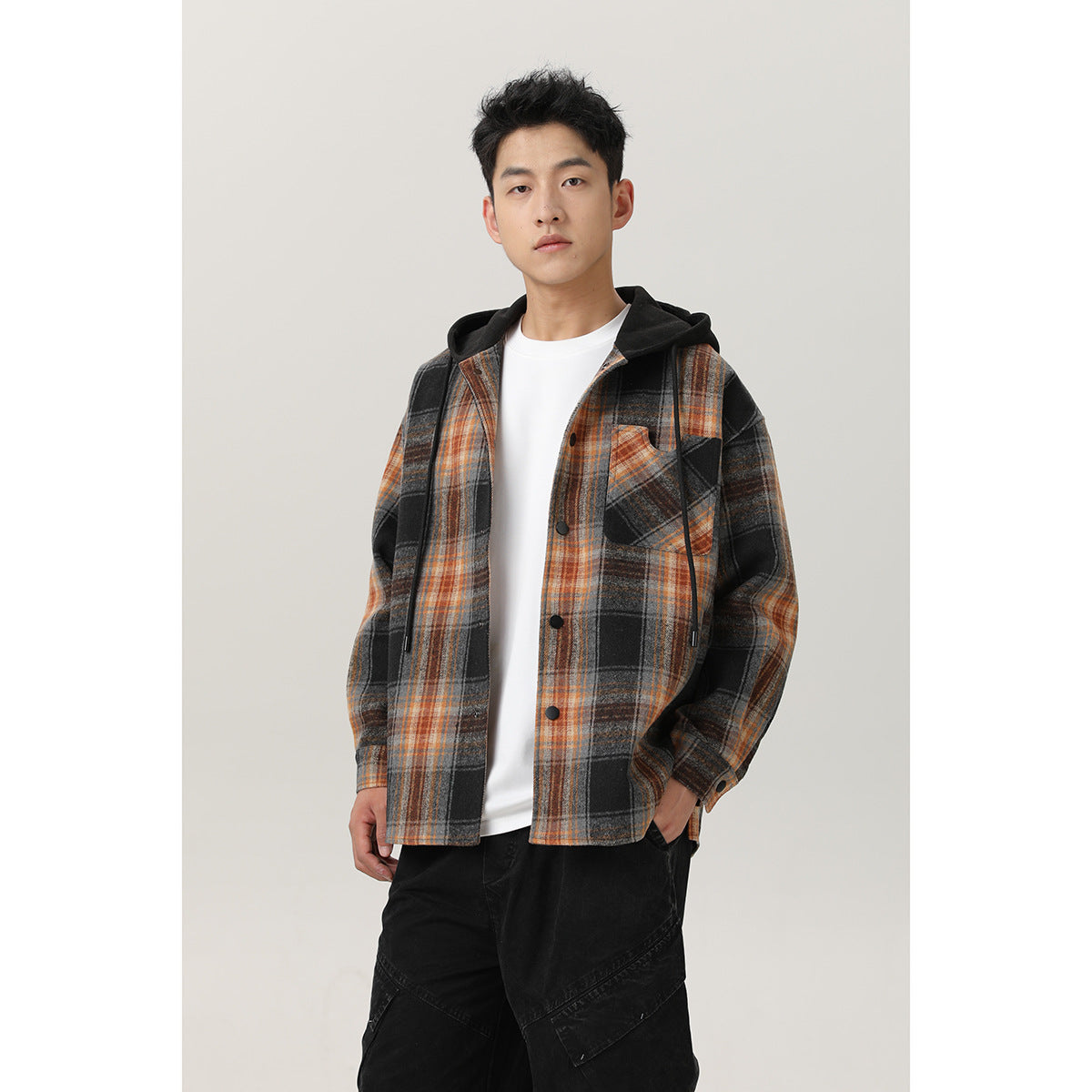 Front view of a man wearing a black, gray, and orange plaid hooded overshirt over a white shirt.