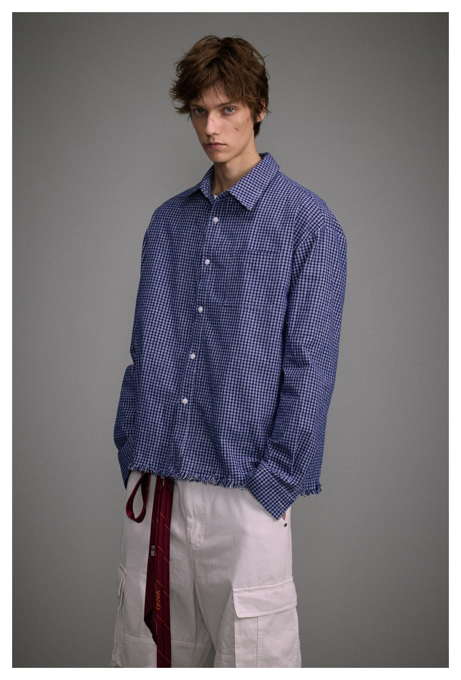 Three-quarter view of a model wearing a blue checked button-up shirt with a frayed hem.