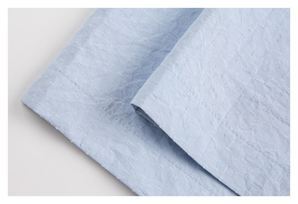 Close-up of the pale blue shirt's folded hem and stitching against a light background.