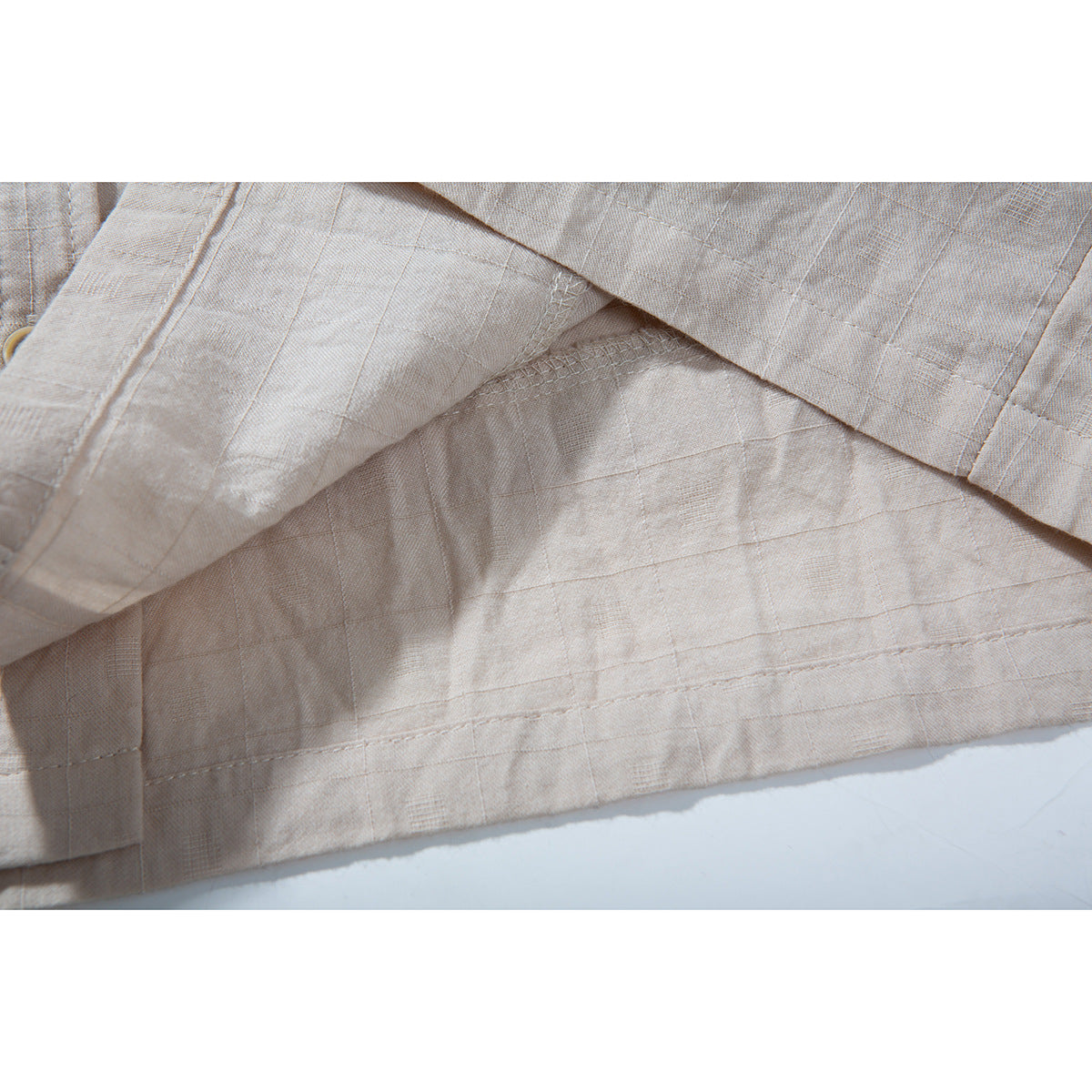 Close-up of pale beige shirt fabric showing a subtle grid weave, seams, and stitching.