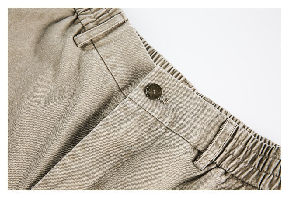 Close-up of beige pants showing the button closure, belt loop, and gathered elastic waistband.