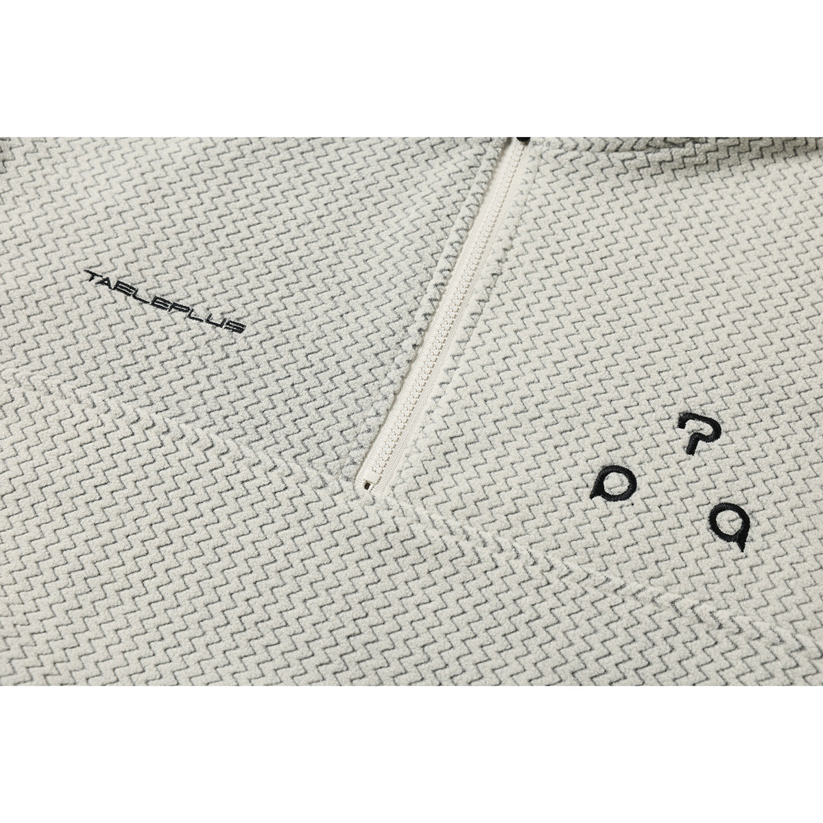 Close-up of cream zigzag-patterned fabric showing a white zipper and small black chest embroidery.