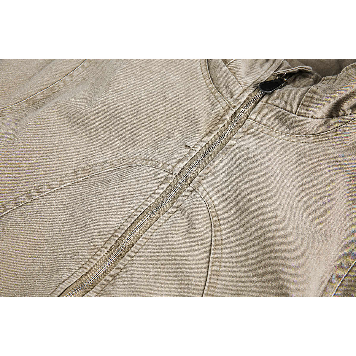 Close-up of a tan jacket's metal front zipper, black pull, and curved panel stitching.