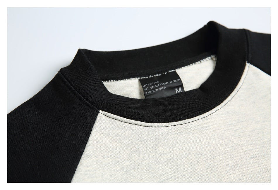Close-up of the black ribbed crew neck, raglan seam and interior size label on an off-white and black sweatshirt.
