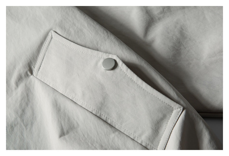 Close-up of a pale gray jacket's sleeve tab with a round snap button.