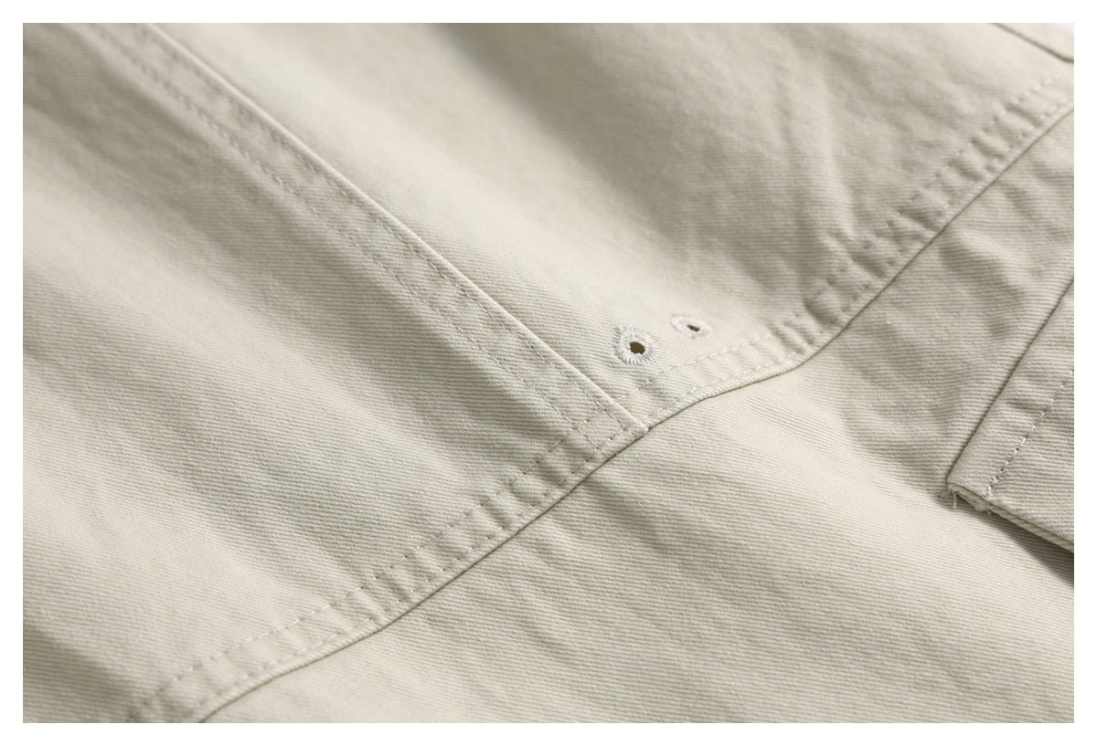 Close-up of light beige trousers showing two stitched buttonholes and intersecting seams.