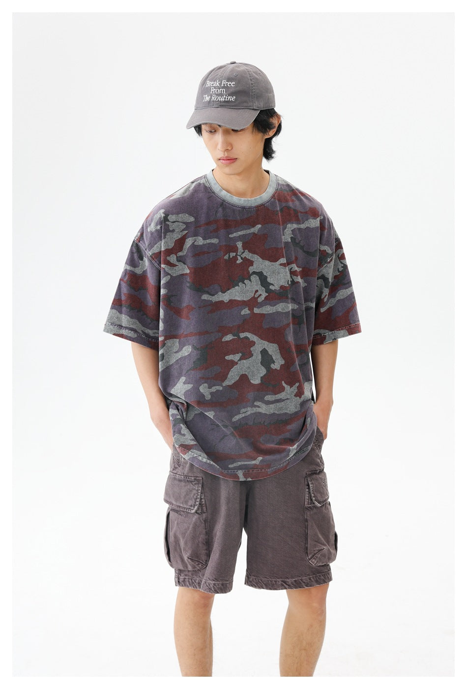 Closer view of a model wearing an oversized burgundy, gray and charcoal camouflage T-shirt with gray cargo shorts.