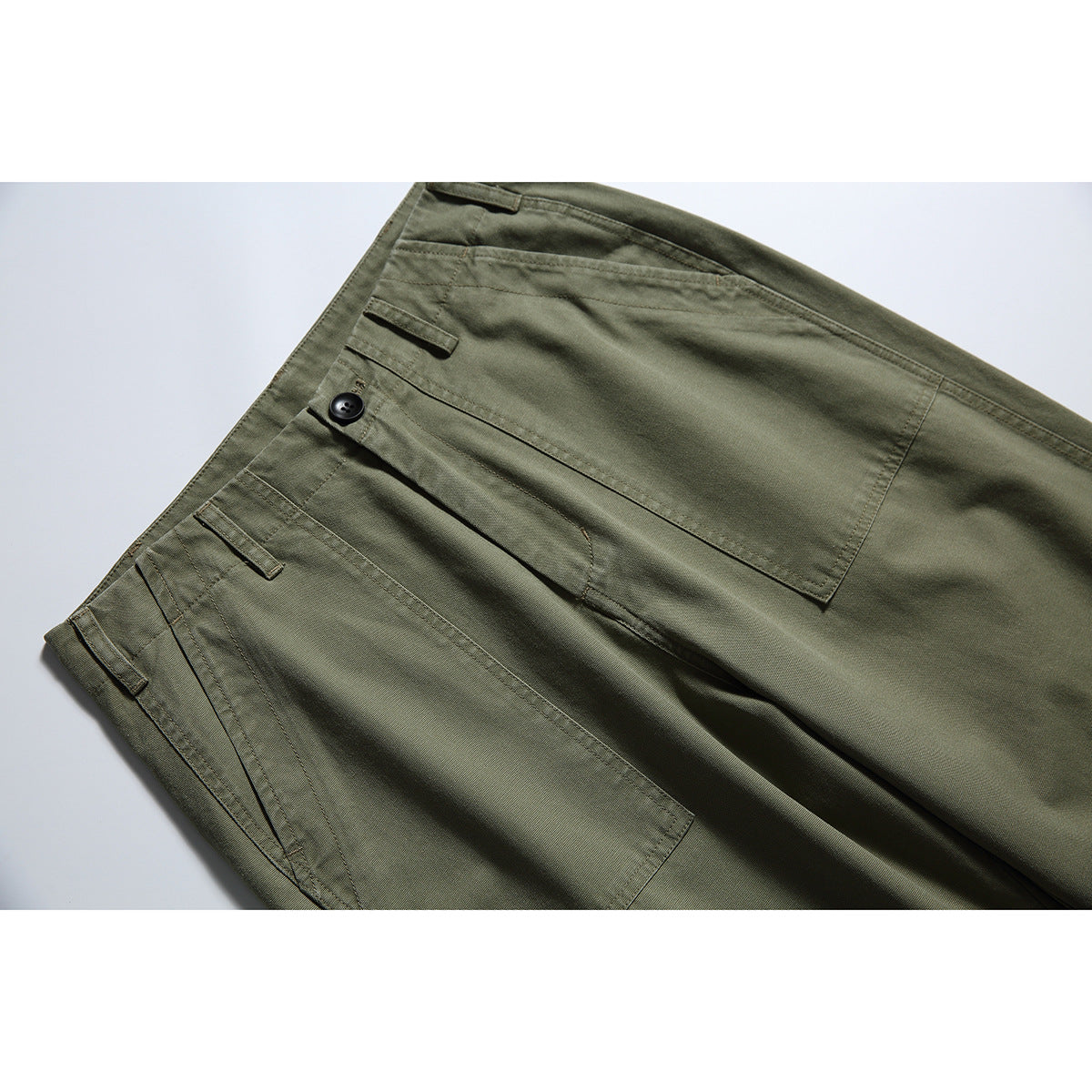 Close-up of olive-green trousers showing the waistband, button, belt loops and large front pockets.