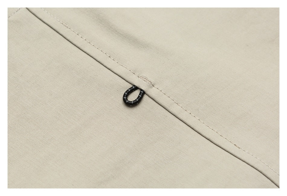 Close-up of beige garment fabric with a small black loop attached beside a stitched seam.