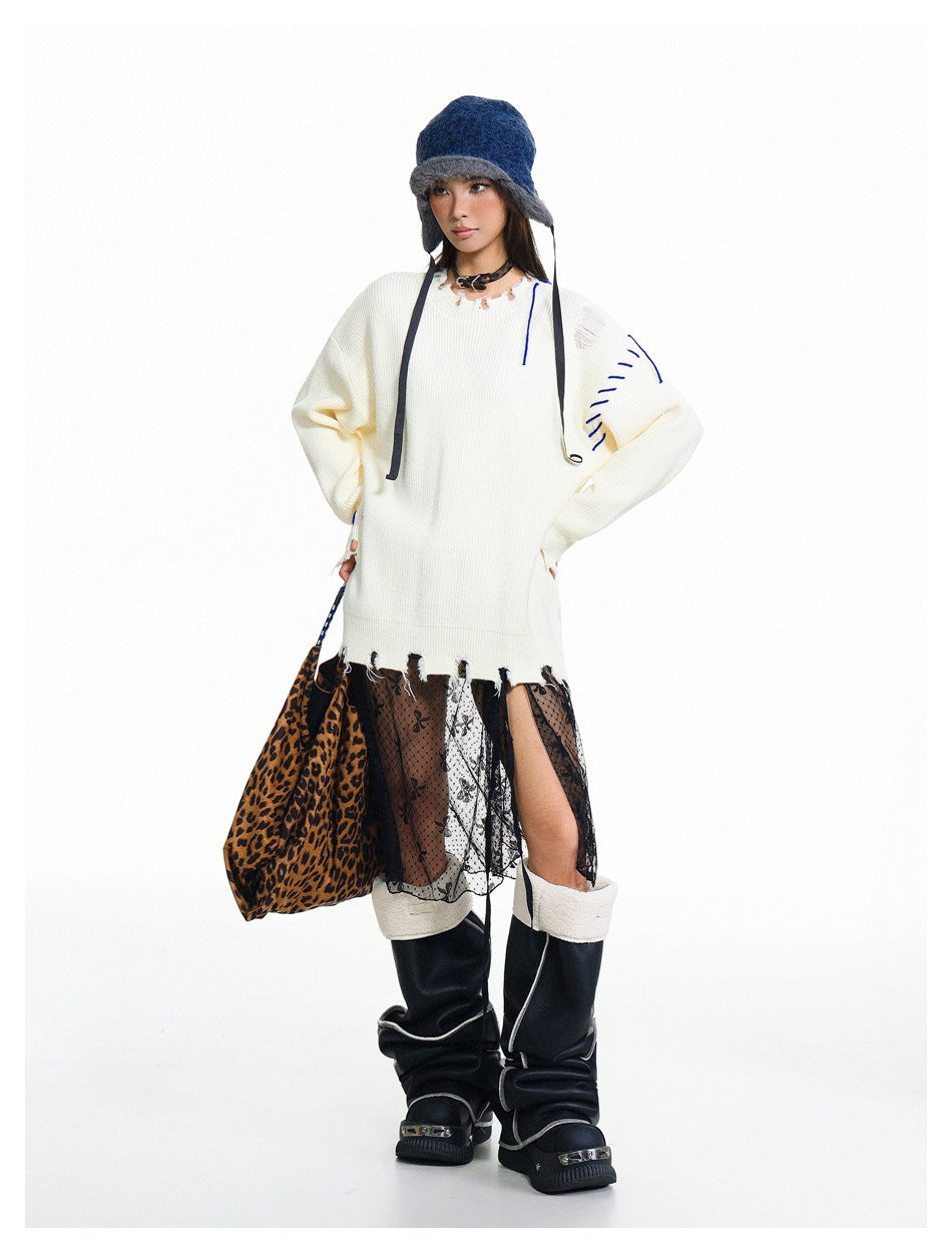 Full-length model wearing an oversized ivory distressed sweater with blue stitching, a sheer patterned skirt, and black