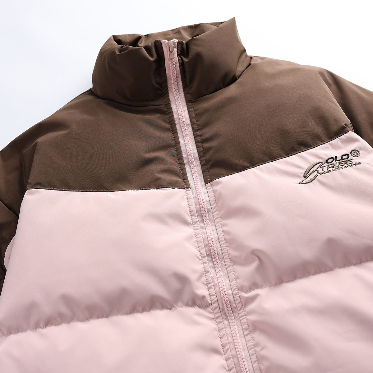 Close-up of a brown and pale pink color-block puffer jacket front, showing its high collar, pink zipper and embroidered chest