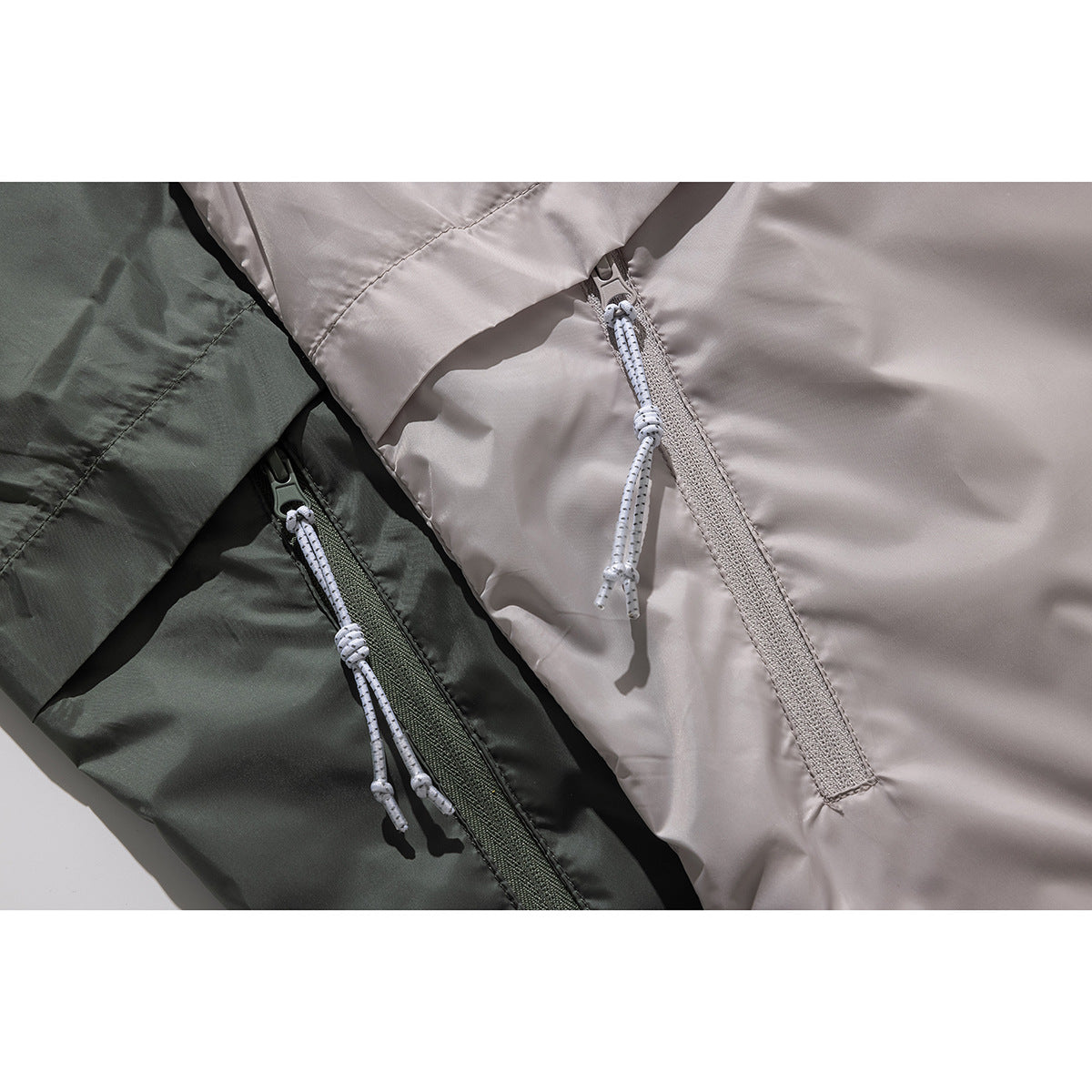 Close-up comparing light taupe and dark olive jackets, with front zippers and white cord pulls.