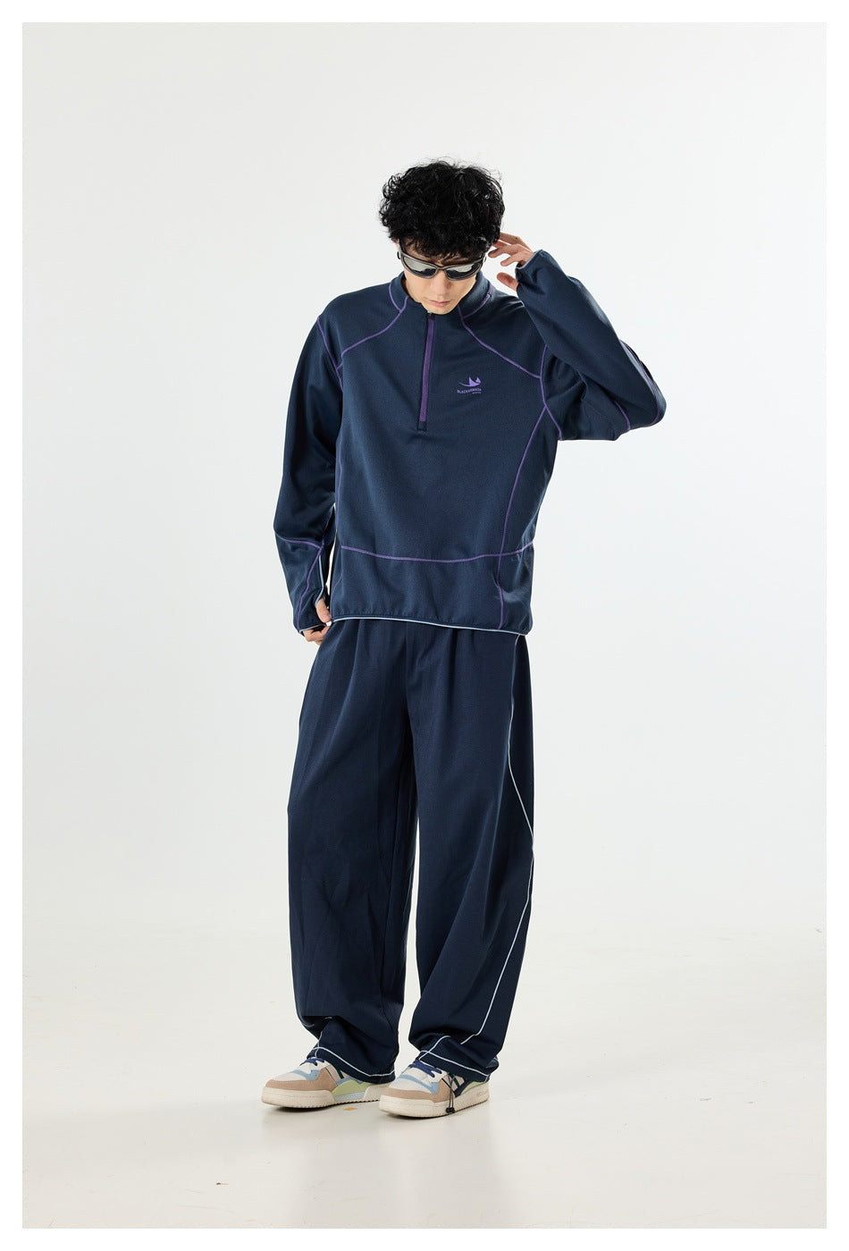 Model wearing a navy quarter-zip pullover with purple seams and matching wide-leg trousers, looking down.
