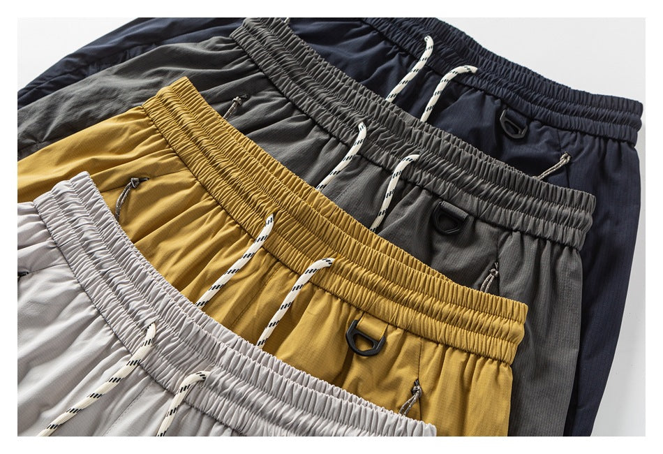Several pairs of drawstring pants in light gray, mustard, charcoal, and navy arranged together.