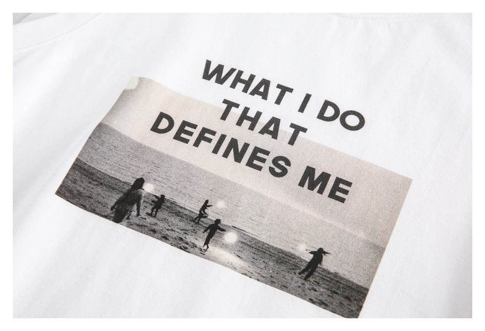 Close-up of a white top printed with “WHAT I DO THAT DEFINES ME” above a black-and-white beach scene.